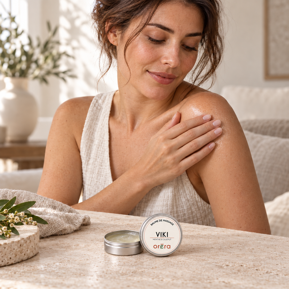 Une femme applique le baume VIKI sur son épaule, avec le petit pot ouvert posé devant elle.