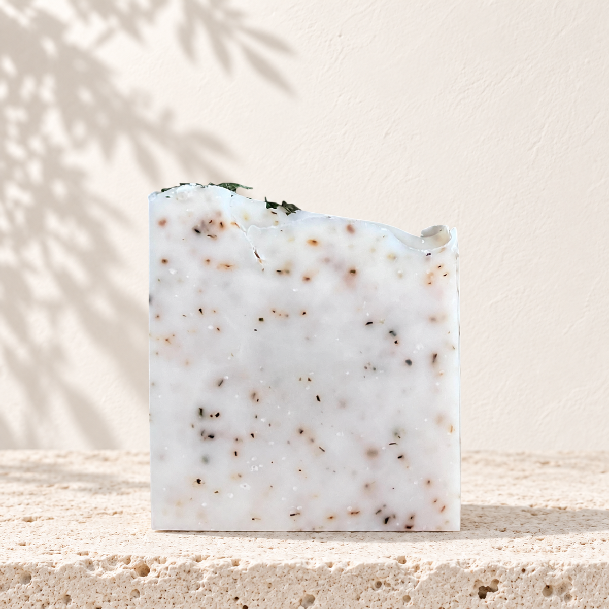 Savon exfoliant blanc marbré avec grains bruns, forme carrée irrégulière, naturel.