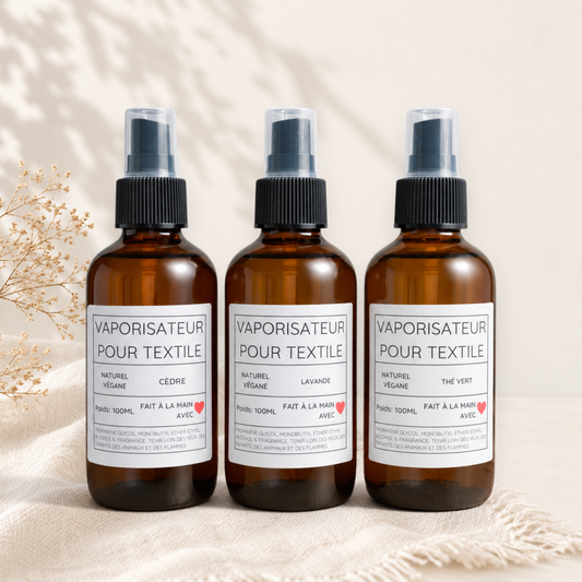 Trois vaporisateurs textile ambrés à pulvérisateur noir, étiquettes blanches minimalistes, parfum coton, lavande, thé vert.