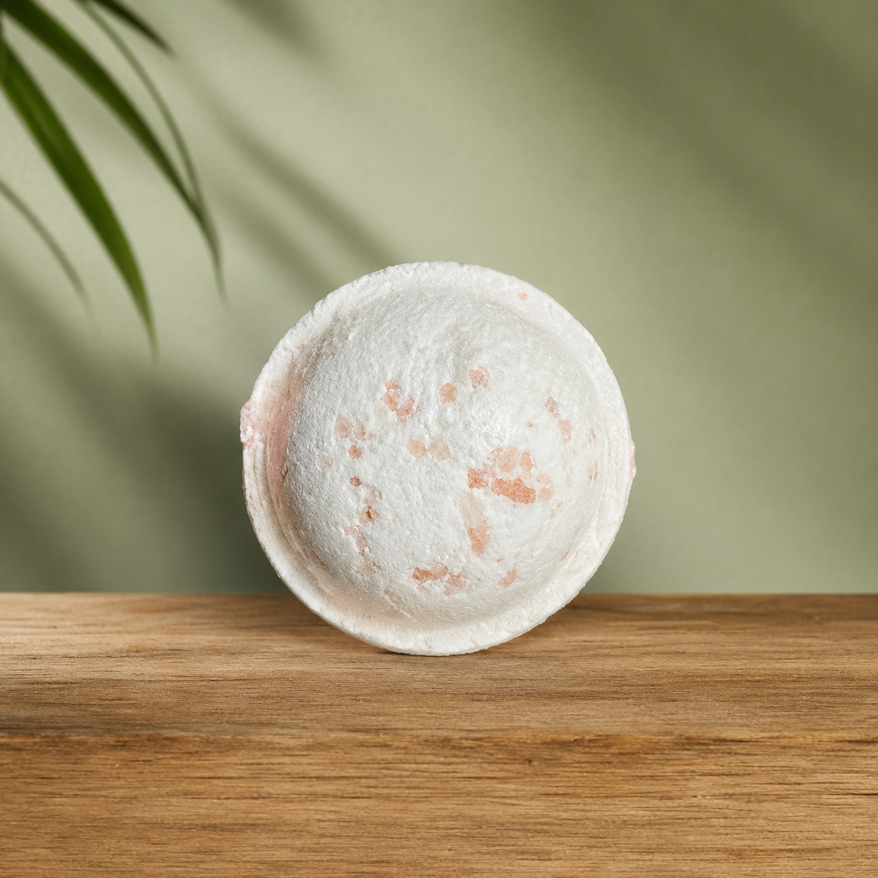 Bombe de bain ronde blanche avec éclats rosés sur plateau en bois clair.