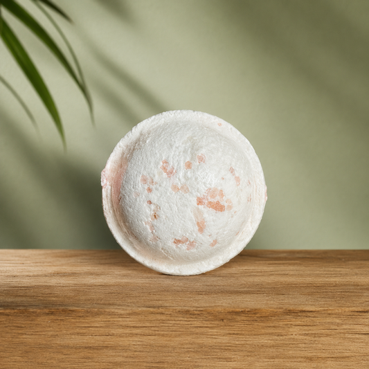 Bombe de bain ronde blanche avec éclats rosés sur plateau en bois clair.