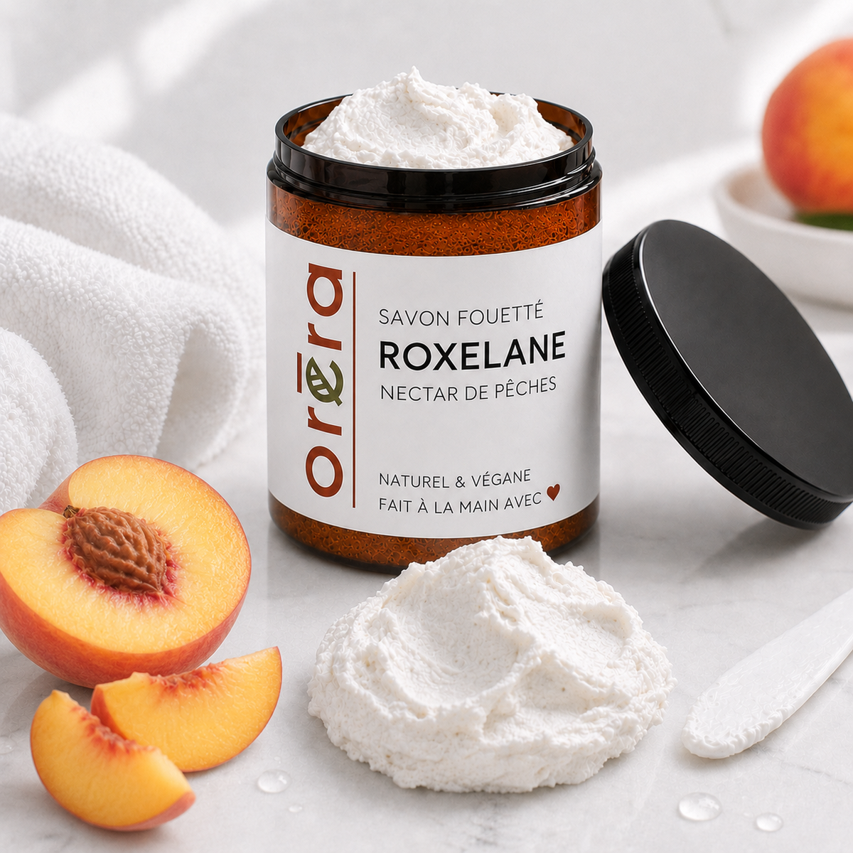 Pot en verre ambré de savon fouetté blanc, étiquette blanche avec texte orange et noir, couvercle noir posé à côté.