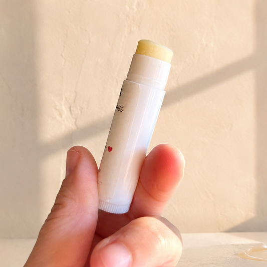 Baume à lèvres blanc au baume cacao karité naturel dans un tube rond translucide, tenu à la main.