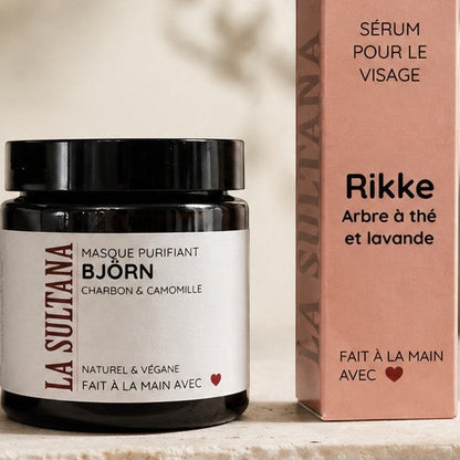 Pot noir mat avec étiquette beige et texte noir, sérum visage Rikke arbre à thé & lavande, boîte beige assortie.