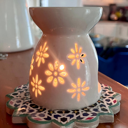 Diffuseur céramique blanc avec motifs floraux lumineux, design épuré et arrondi, ambiance chaleureuse.