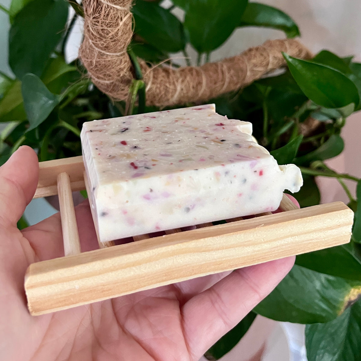 Porte savon en bois naturel tenant un savon blanc moucheté de pétales séchés, compact et artisanal.