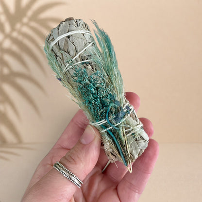 Sauge blanche liée avec brins de végétaux verts et bleus, décor naturel et artisanal.