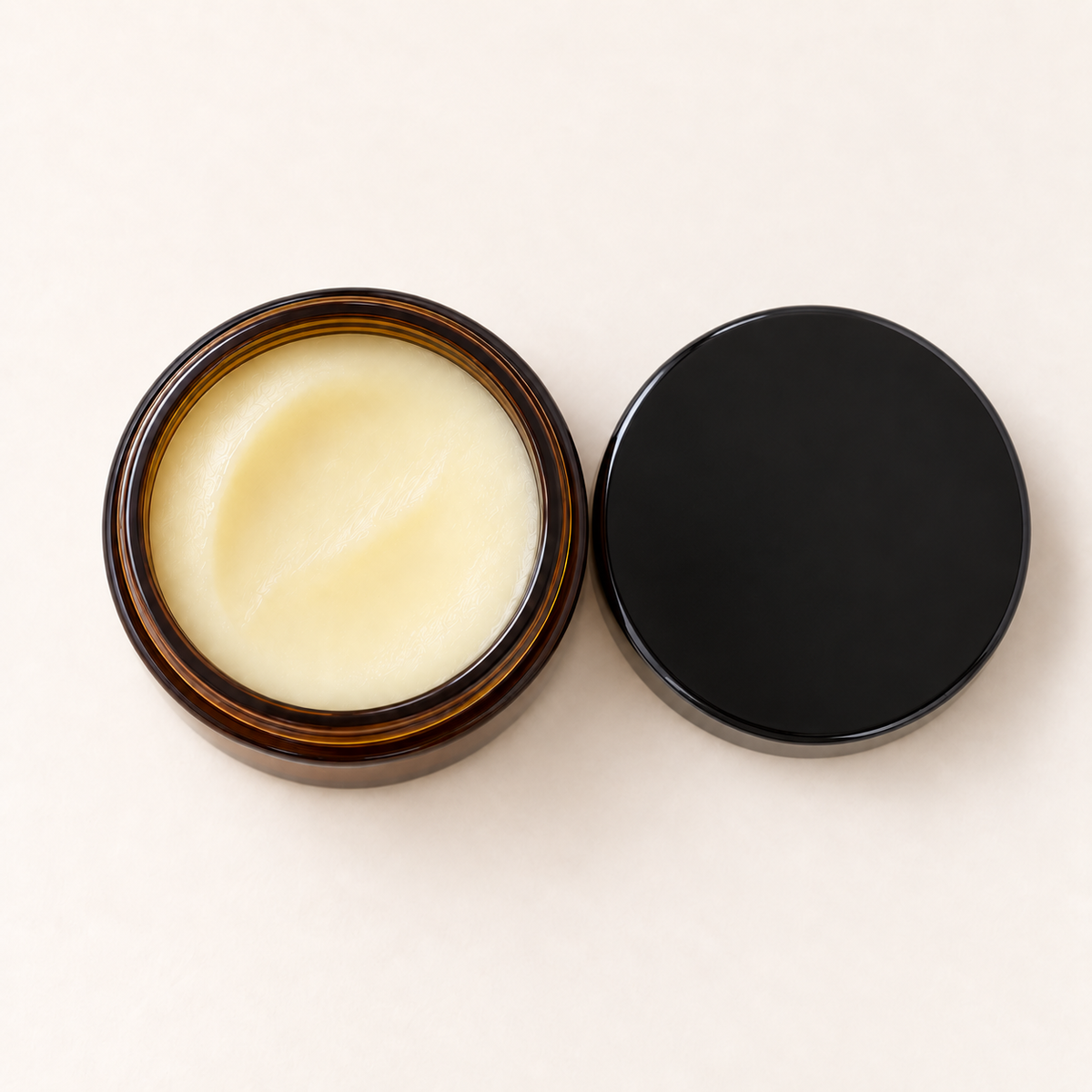 Pot en verre ambré ouvert avec baume jaune pâle et couvercle noir posé à côté.