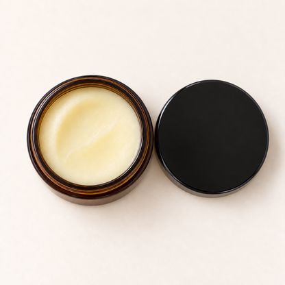 Pot en verre ambré ouvert avec baume jaune pâle et couvercle noir posé à côté.