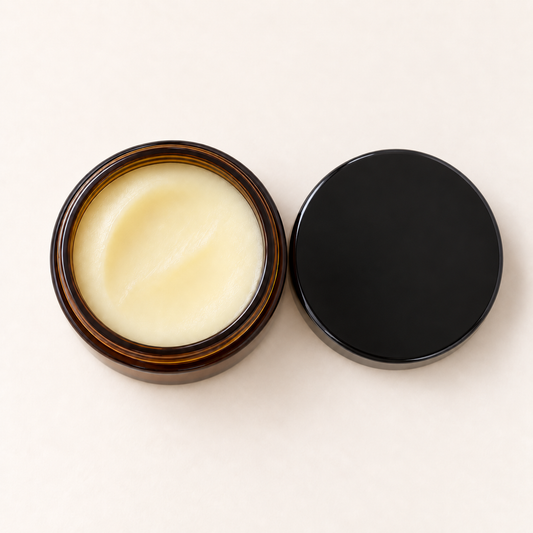 Pot en verre ambré ouvert avec baume jaune pâle et couvercle noir posé à côté.