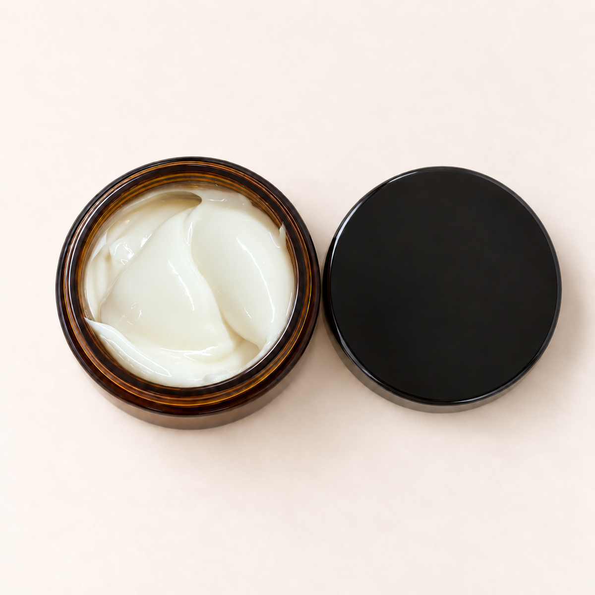 Pot en verre ambré ouvert avec crème hydratante blanche, couvercle noir mat posé à côté.