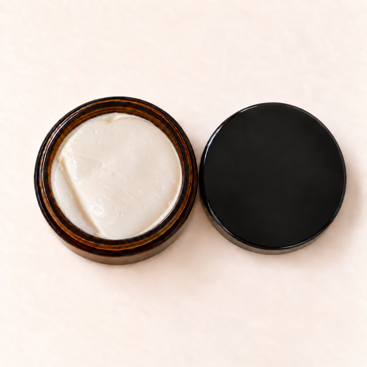 Pot en verre ambré avec crème blanche hydratante, couvercle noir mat posé à côté.