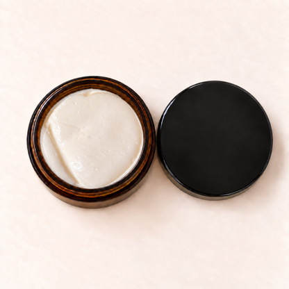 Pot en verre ambré avec crème blanche hydratante, couvercle noir mat posé à côté.