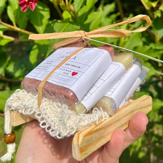 Ensemble de savons artisanaux rose et blanc avec éponge en crochet et porte-savon en bois naturel.