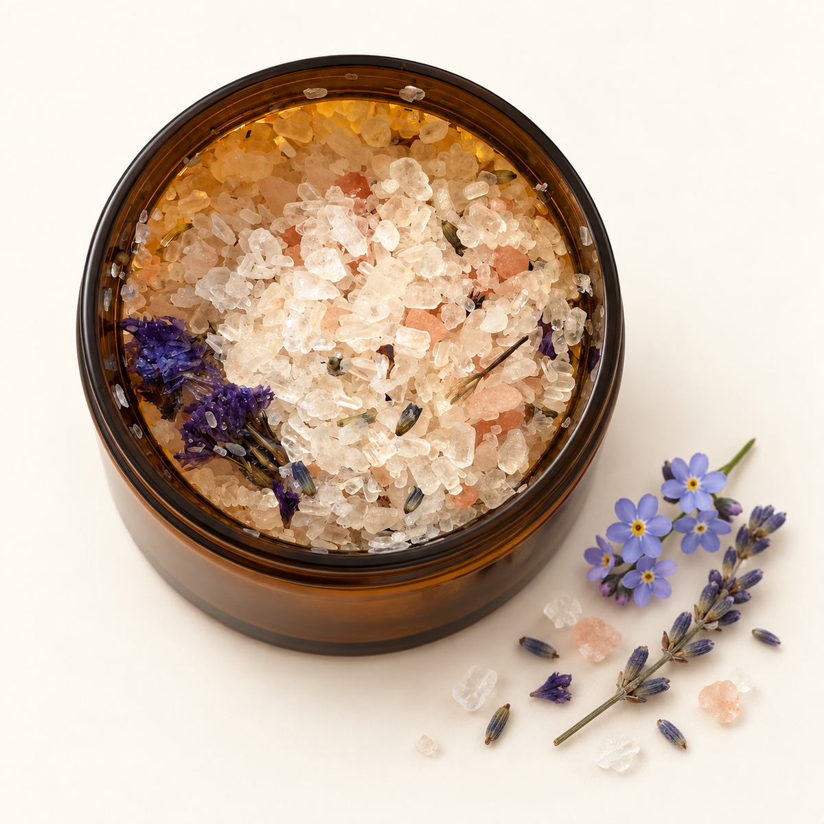 Pot en verre ambré rempli de sels botaniques transparents avec fleurs de lavande et myosotis, décor délicat.