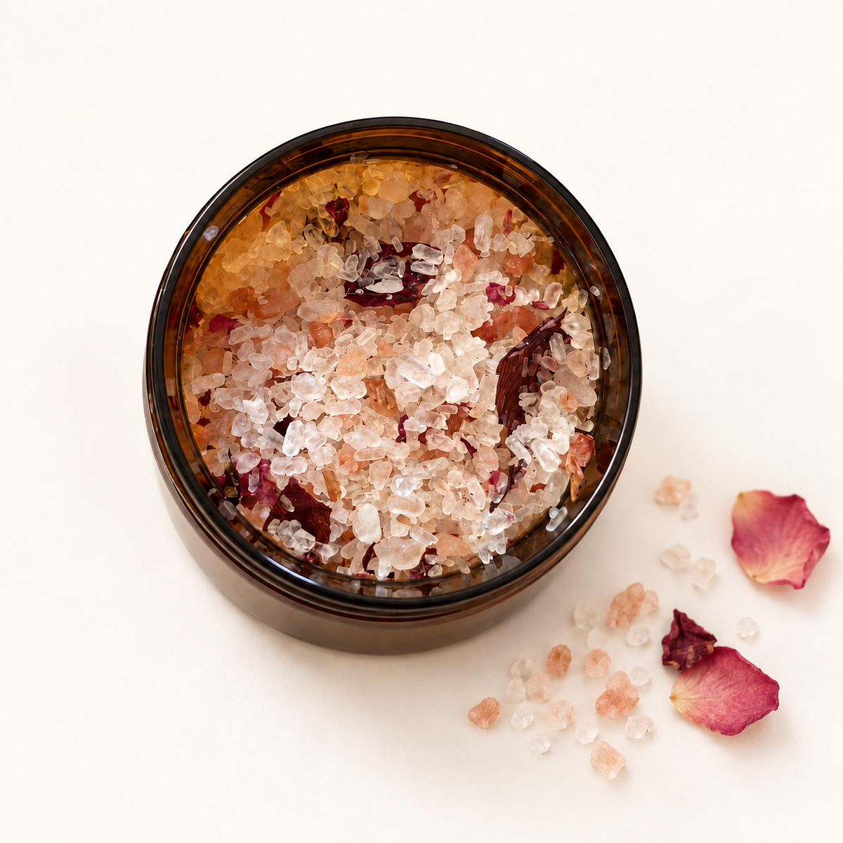 Pot en verre brun rempli de sels de bain roses avec pétales de rose séchés.