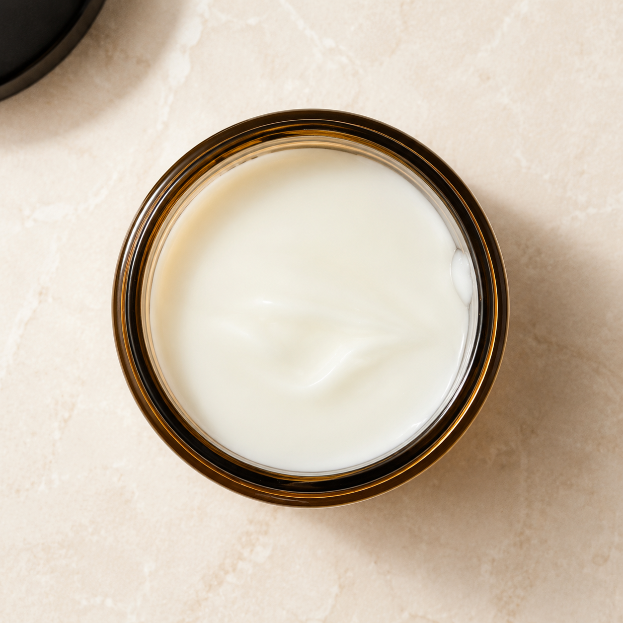 ORERA Pot en verre ambré rempli d’un lait nettoyant visage blanc crémeux.
