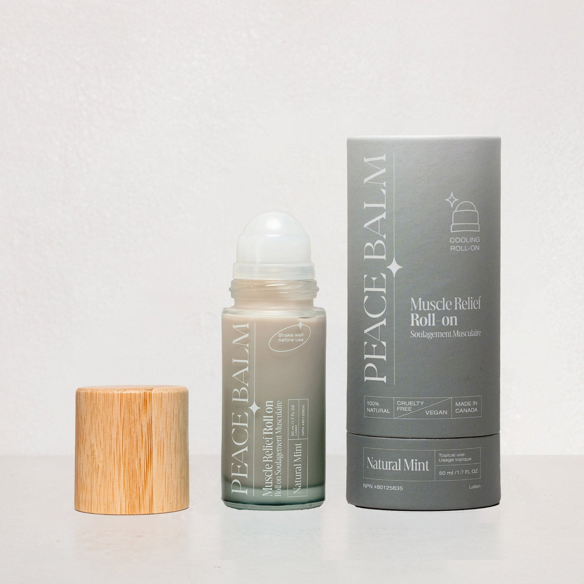 Baume Peace Balm vert clair à bille rouleau, emballage gris cartonné avec texte blanc, bouchon en bois naturel.