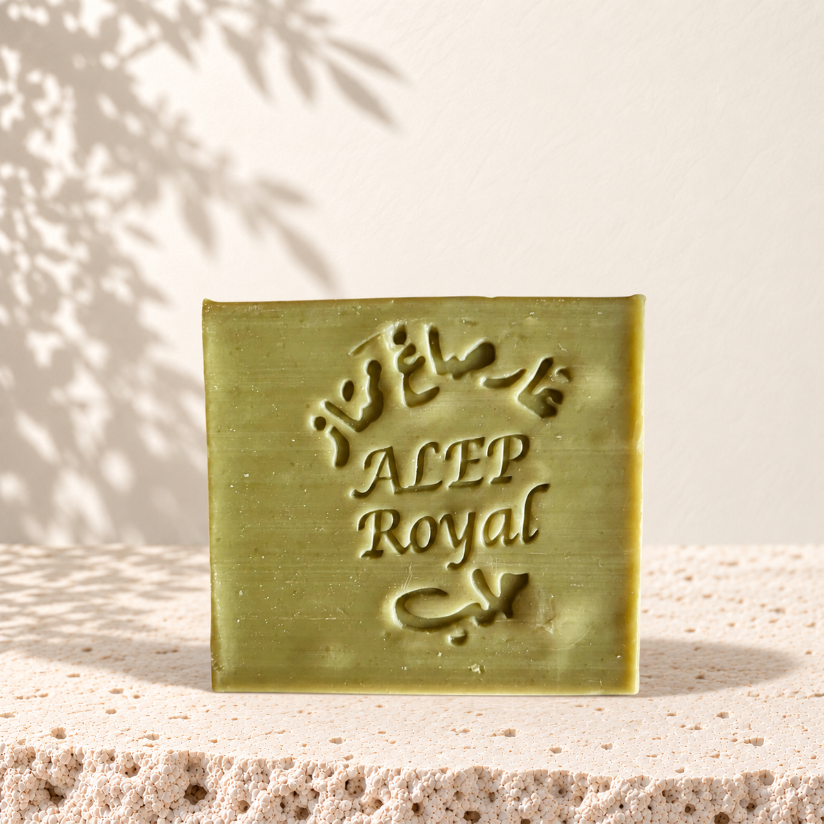 Savon carré vert olive marqué Alep Royal, texture lisse, posé sur pierre beige texturée.