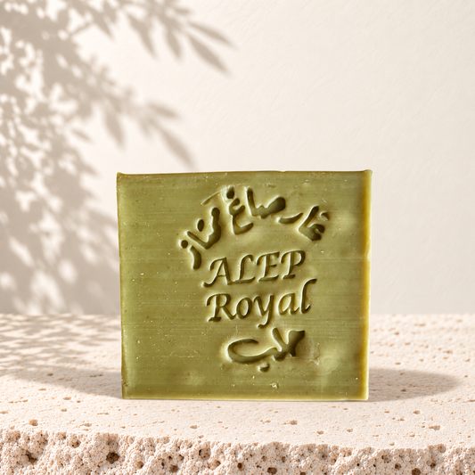 Savon carré vert olive marqué Alep Royal, texture lisse, posé sur pierre beige texturée.