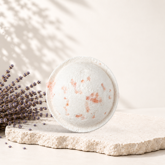 Bombe de bain ronde blanche avec éclats rouges, style artisanal, posée sur pierre beige avec lavande sèche.