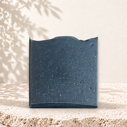 Savon exfoliant rectangulaire noir charbon actif texture granuleuse surface irrégulière.
