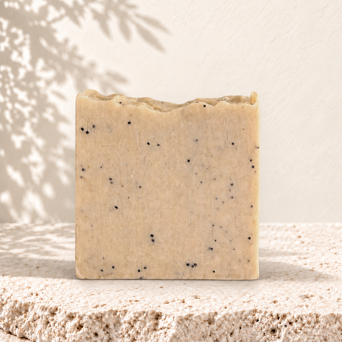 Savon exfoliant carré beige avec graines de pavot noires incrustées, texture naturelle.