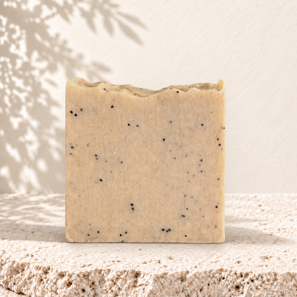 Savon exfoliant carré beige avec graines de pavot noires incrustées, texture naturelle.
