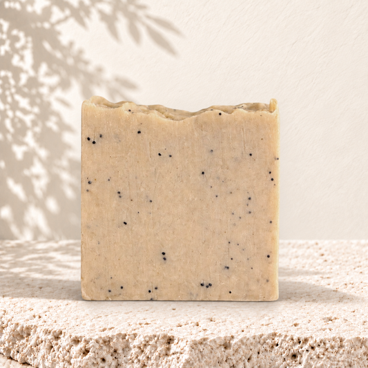 Savon exfoliant carré beige avec graines de pavot noires incrustées, texture naturelle.