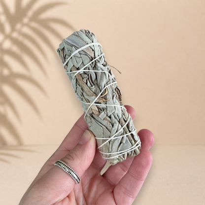Bâton de sauge blanche lié avec de la ficelle, tenu dans une main.