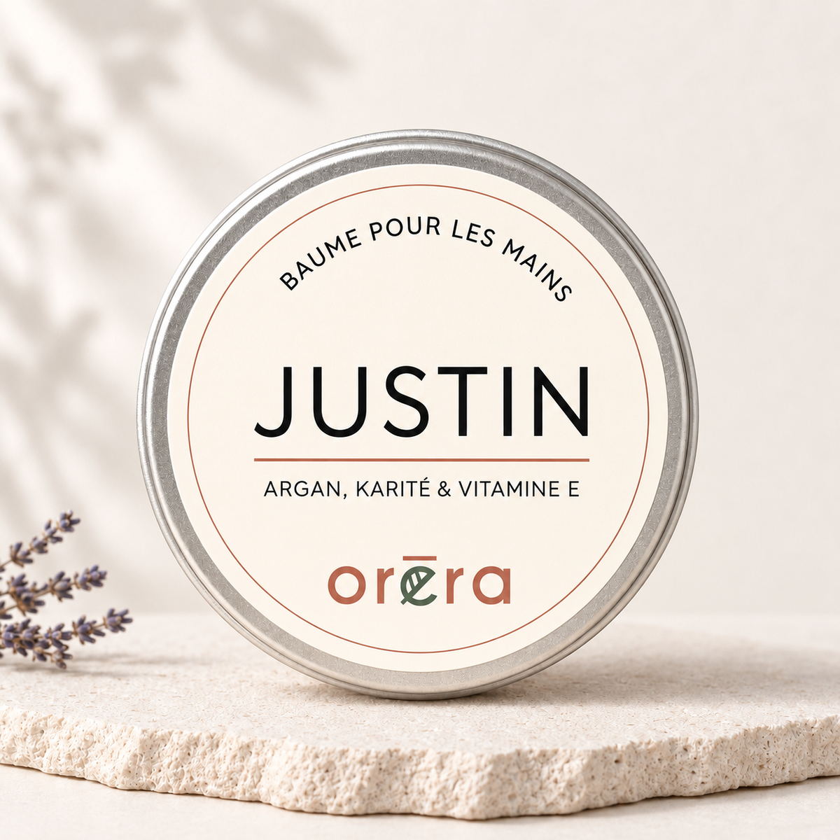 Pot rond métallique de baume pour les mains Justin, étiquette beige avec texte noir et orange.