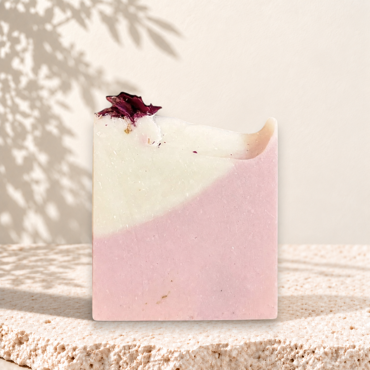Savon rectangulaire rose et blanc à l'argile rose avec pétales de fleurs séchées sur le dessus.