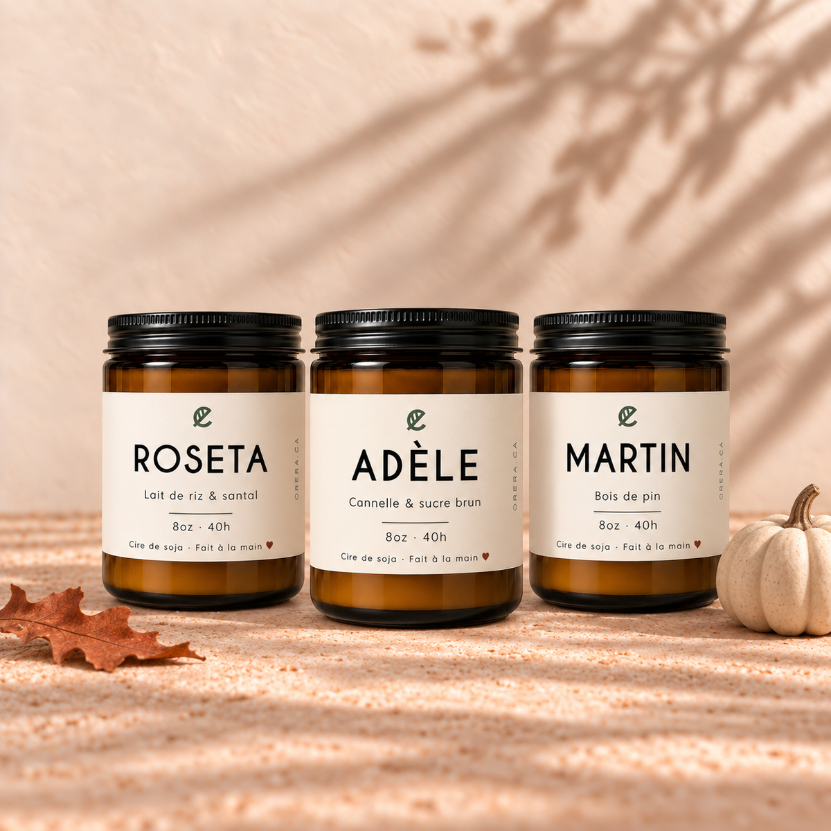 Trois bougies artisanales en verre ambré, étiquettes blanches minimalistes, ADÈLE cannelle et sucre brun au centre.