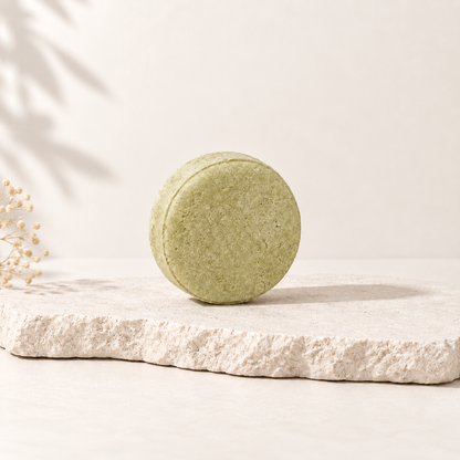 Shampoing solide rond vert clair posé sur pierre beige au style épuré.