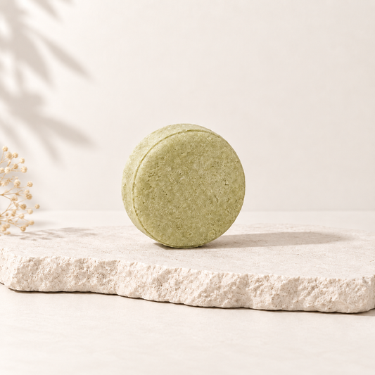 Shampoing solide rond vert clair posé sur pierre beige au style épuré.