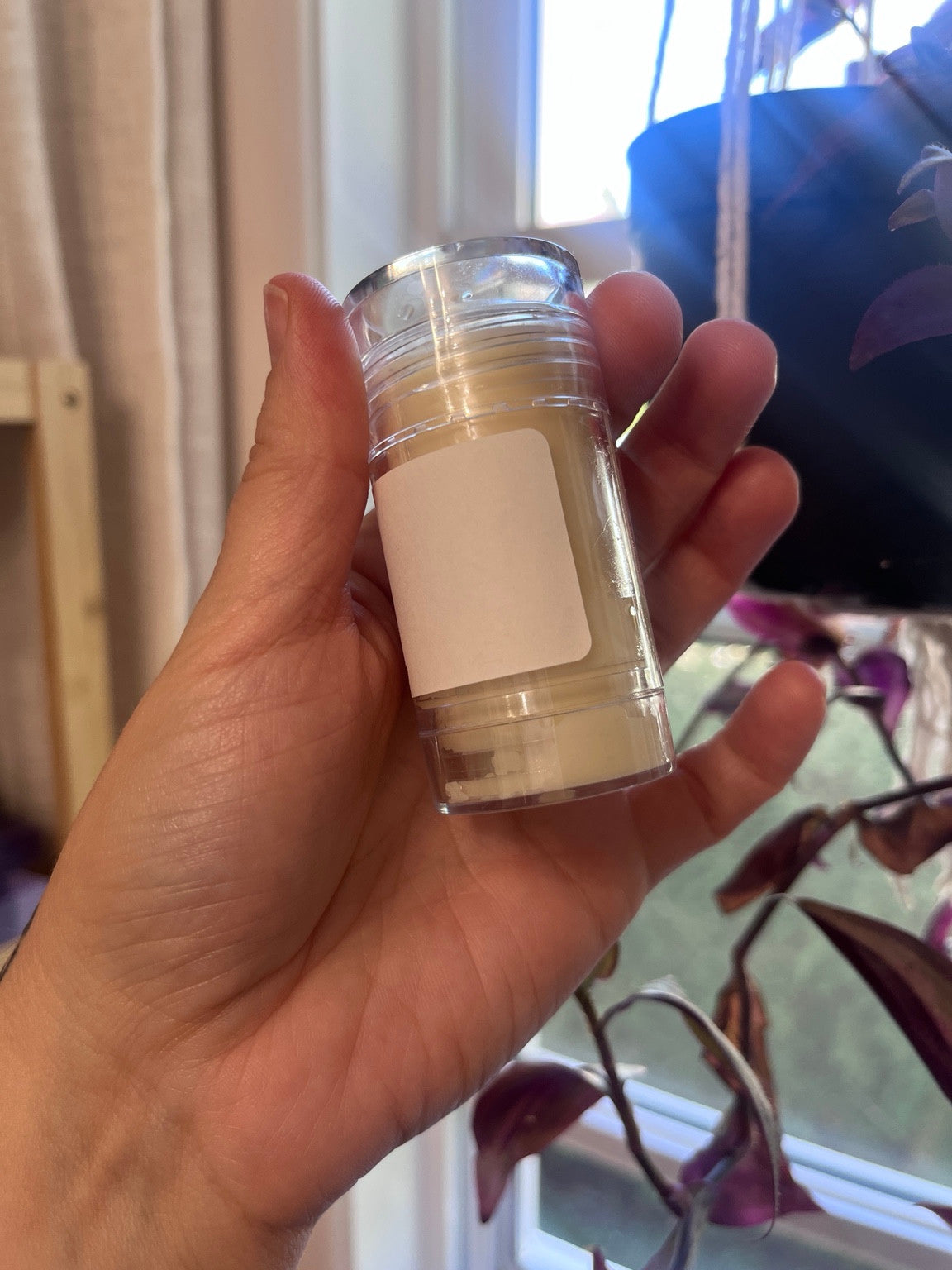 Baume à lèvres CLARA imparfait dans un tube transparent tenu en main, avec un peu de baume visible dans le fond.