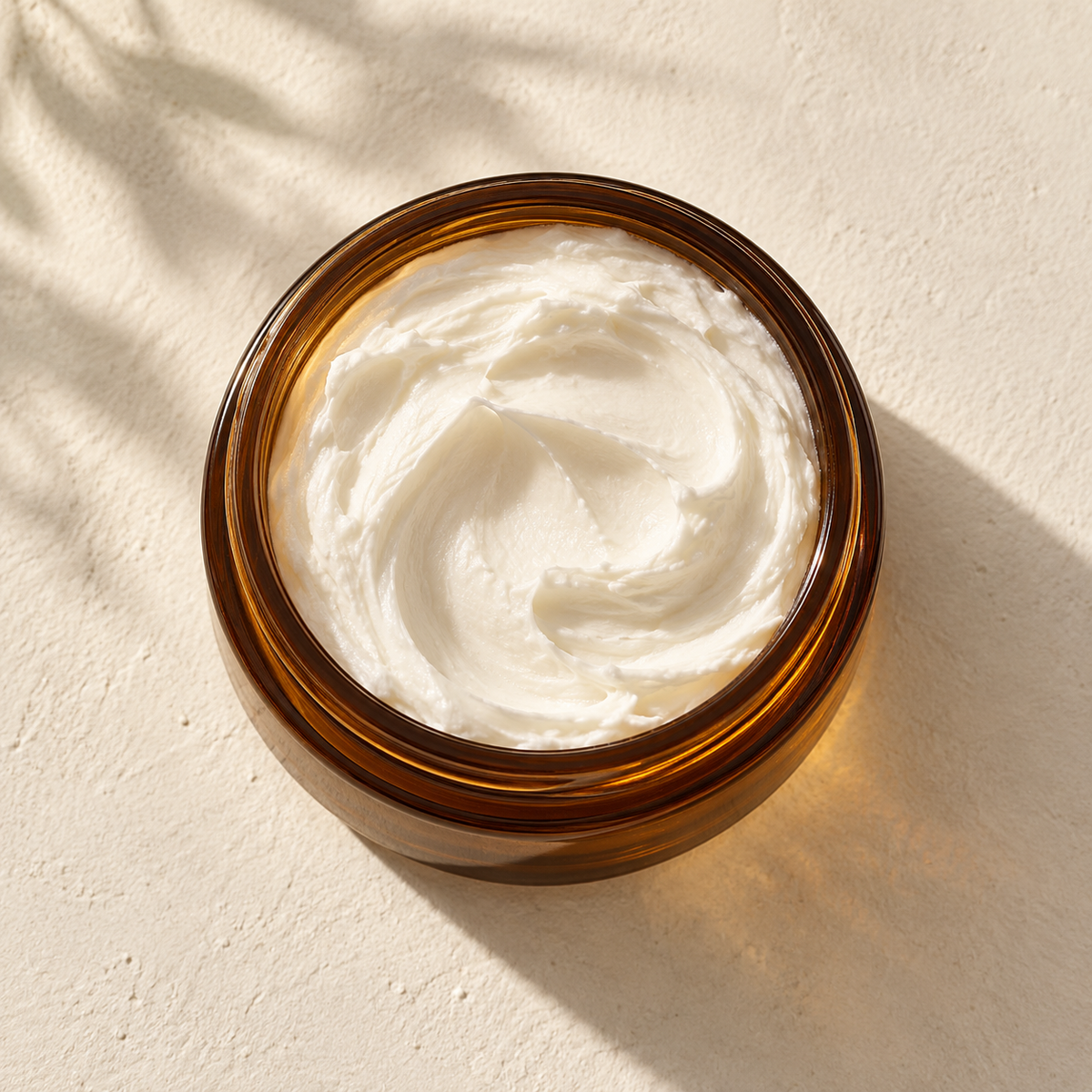 Pot en verre ambré ouvert avec crème blanche onctueuse lisse à l'intérieur, posé sur surface claire.