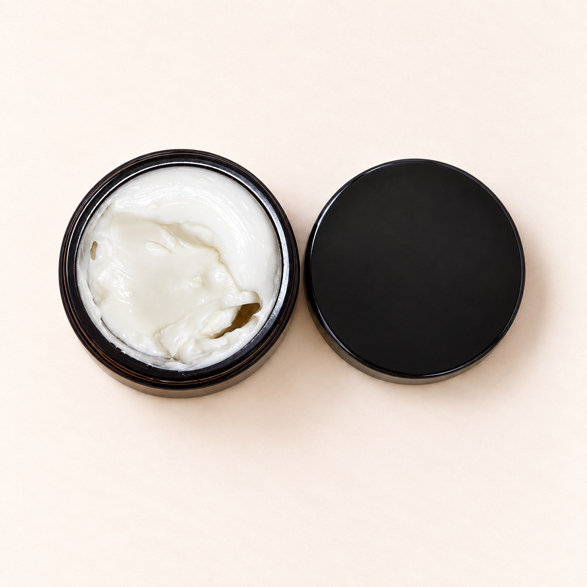Pot en verre ambré ouvert avec crème blanche onctueuse et couvercle noir mat posé à côté.