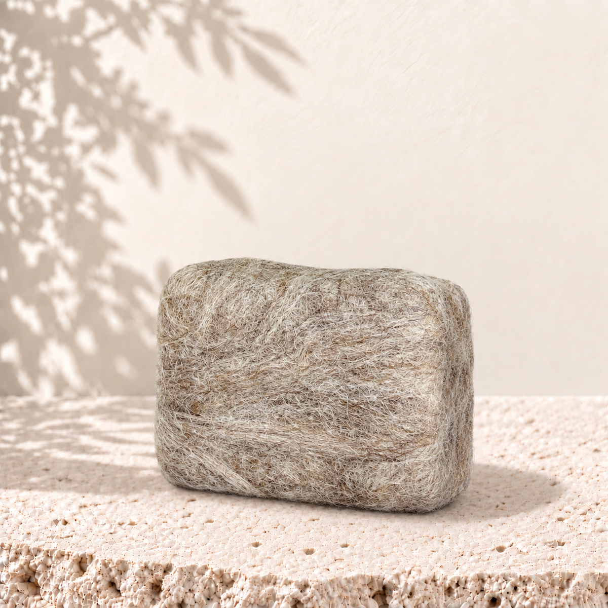Savon rectangulaire beige enveloppé de laine feutrée d'alpaga, texture douce et naturelle.