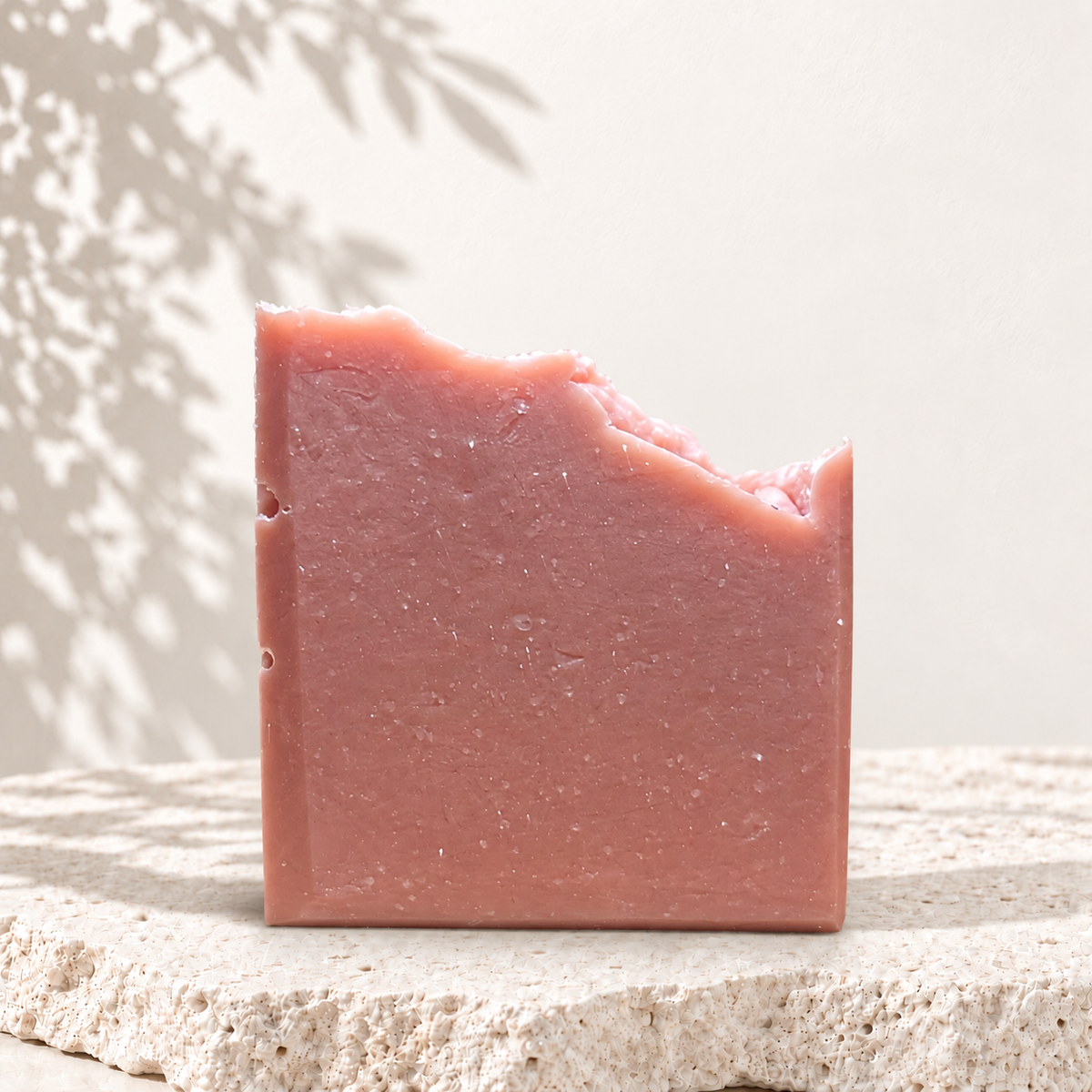 Savon FRIDA rose uni à la texture artisanale, sur la dalle claire et le fond à ombres de feuillage de la collection Oréra.