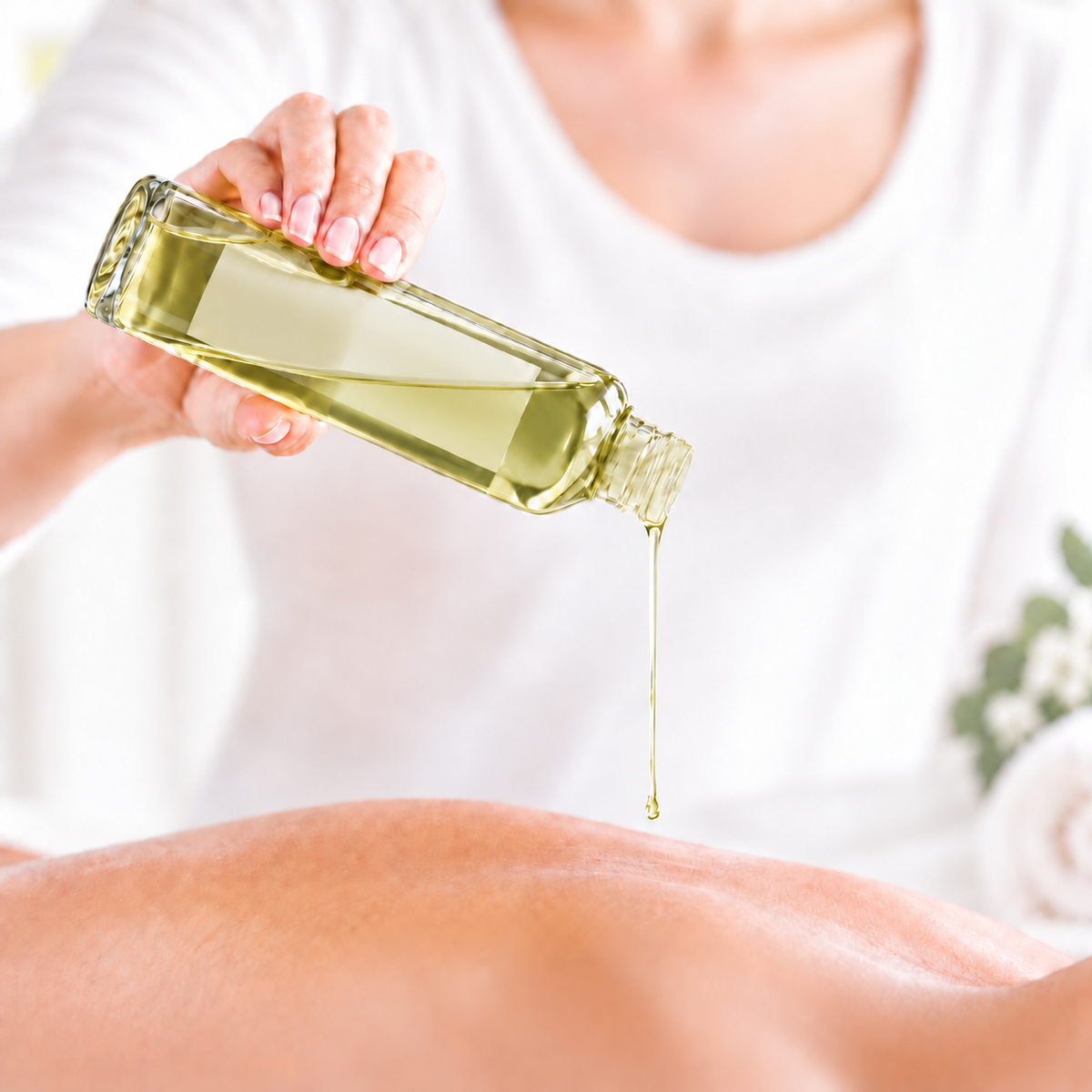 Huile de massage jaune clair versée d’une bouteille en verre transparent sur un dos nu pâle.