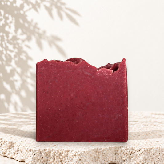 Savon artisanal rectangulaire couleur rose profond avec texture granuleuse, bord irrégulier.