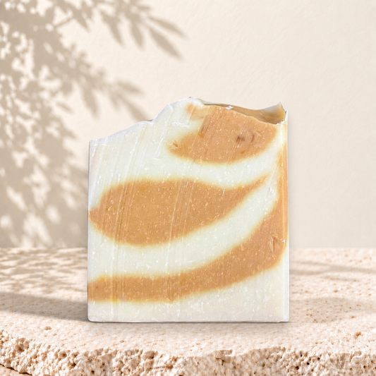 Savon artisanal carré avec marbrures blanc crème et orange doux, aspect naturel.