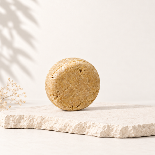 Shampoing solide rond beige en texture naturelle posé sur pierre brute, ambiance épurée.