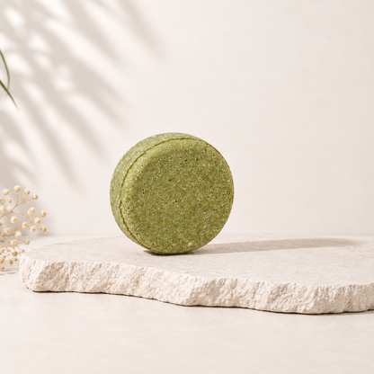 Shampoing solide rond vert mousse, texture fine, posé sur pierre beige naturel.