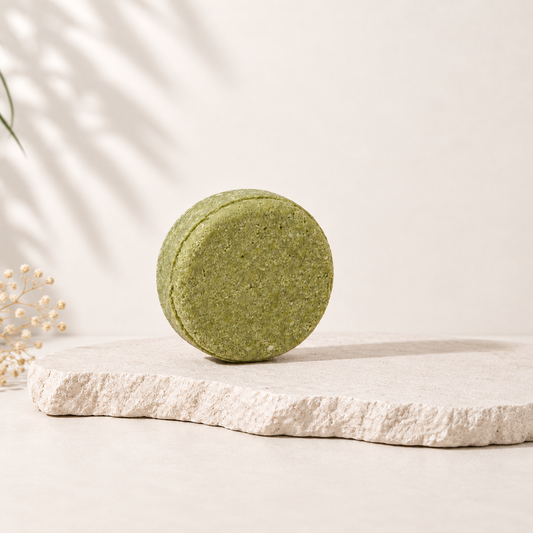 Shampoing solide rond vert mousse, texture fine, posé sur pierre beige naturel.