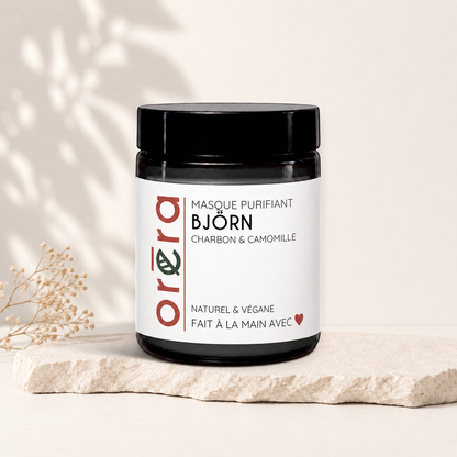 Pot en verre noir avec étiquette blanche et texte noir et rouge, masque visage purifiant charbon camomille.