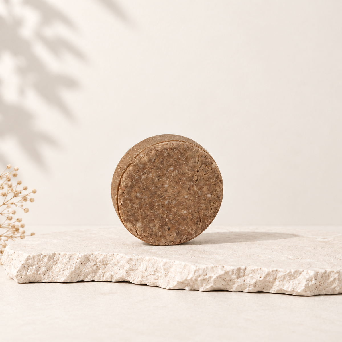 Shampoing solide rond beige texturé pour cheveux fatigués sur pierre claire.