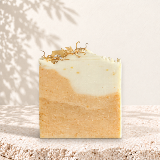 Savon carré bicolore beige et blanc avec éclats de curcuma et fleurs séchées sur le dessus.