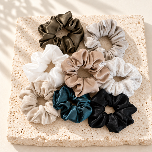 Assortiment de scrunchies en tissus et couleurs variés, posés sur du travertin clair.